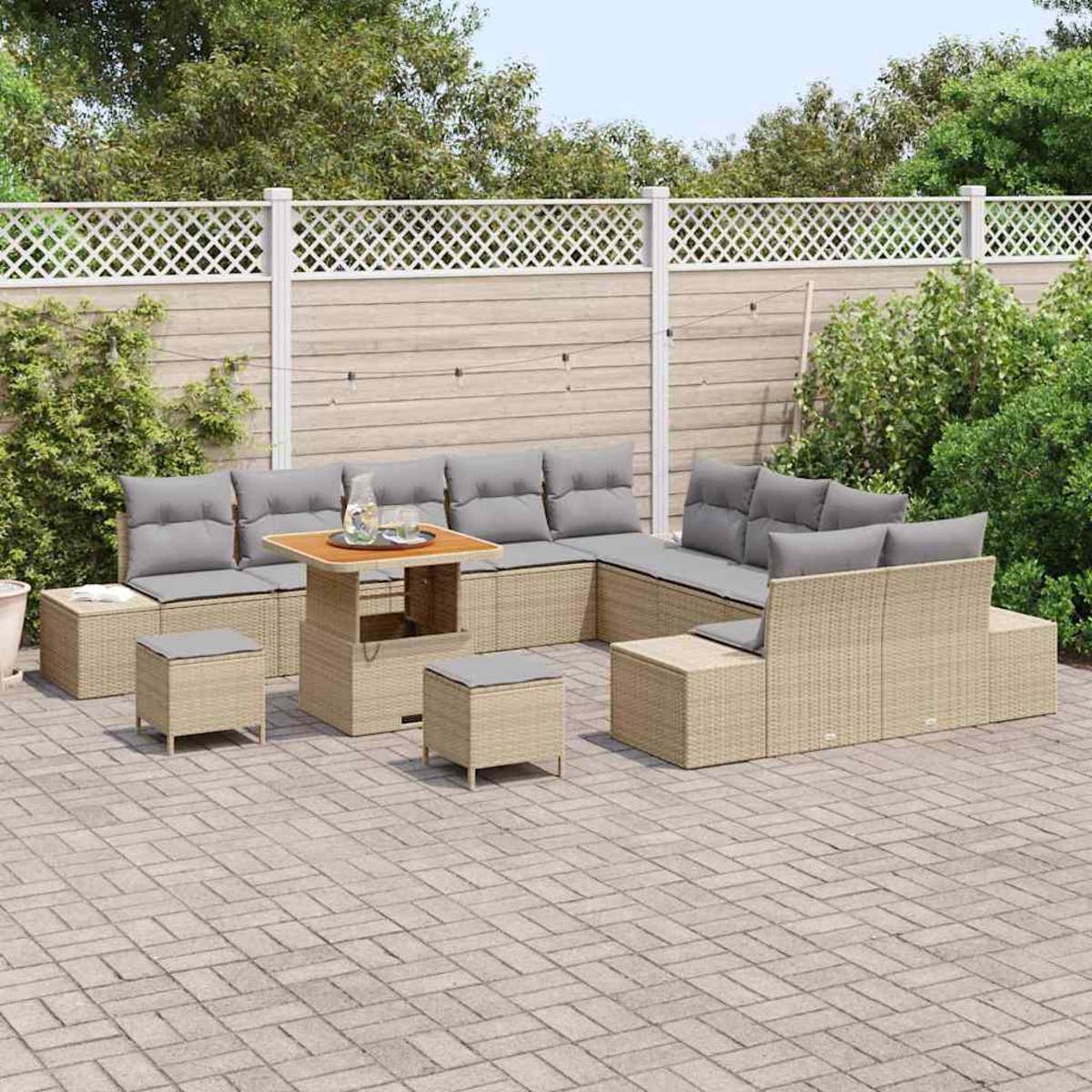Outdoor-Korbsitzgruppe mit grauen Kissen auf einer gepflasterten Terrasse. Holztisch und Hocker. Weißer Gitterzaun und grüne Bäume im Hintergrund.