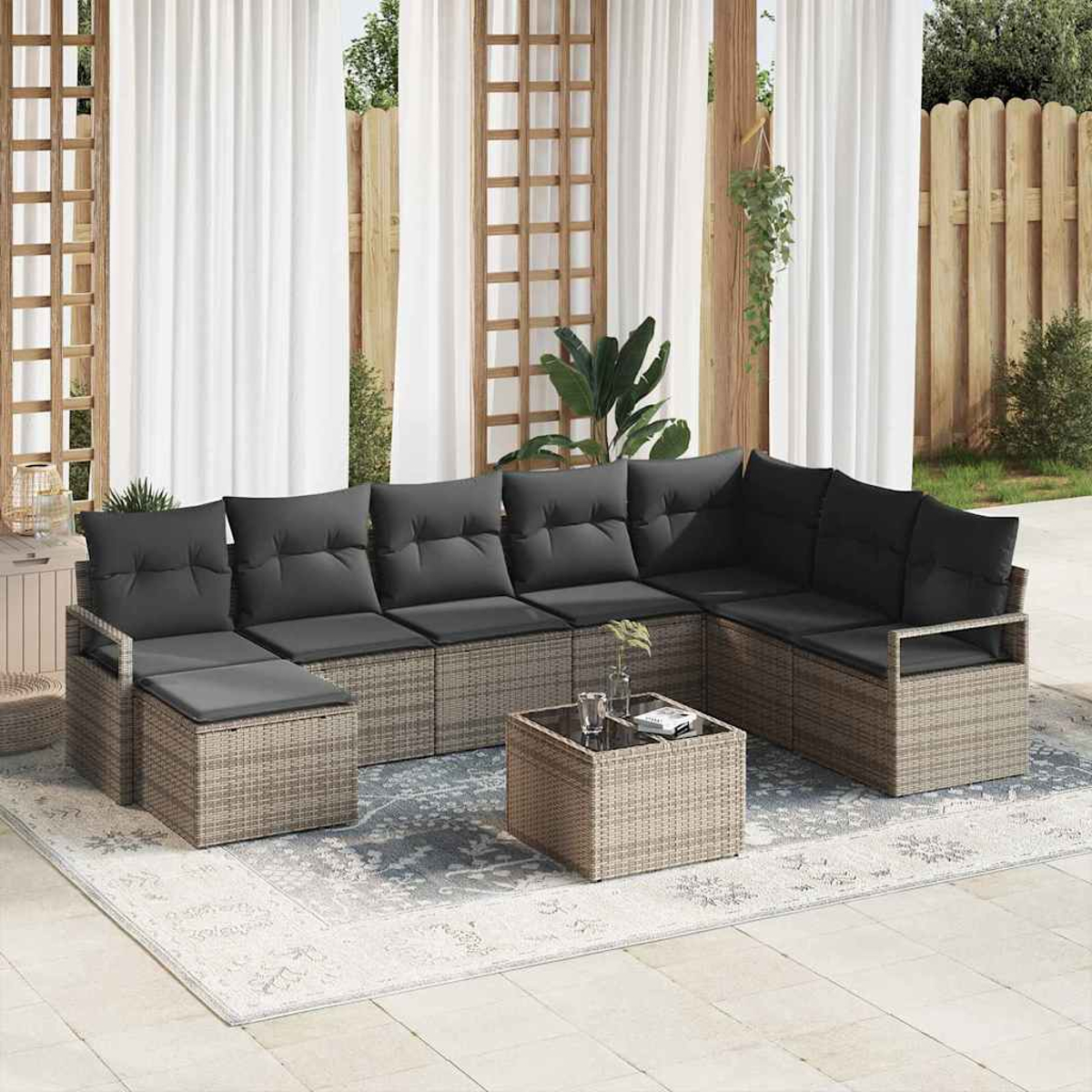 Outdoor-Ecksofa mit schwarzen Kissen und einem kleinen Tisch auf einem Teppich. Der Hintergrund umfasst Vorhänge und einen Holzzaun.