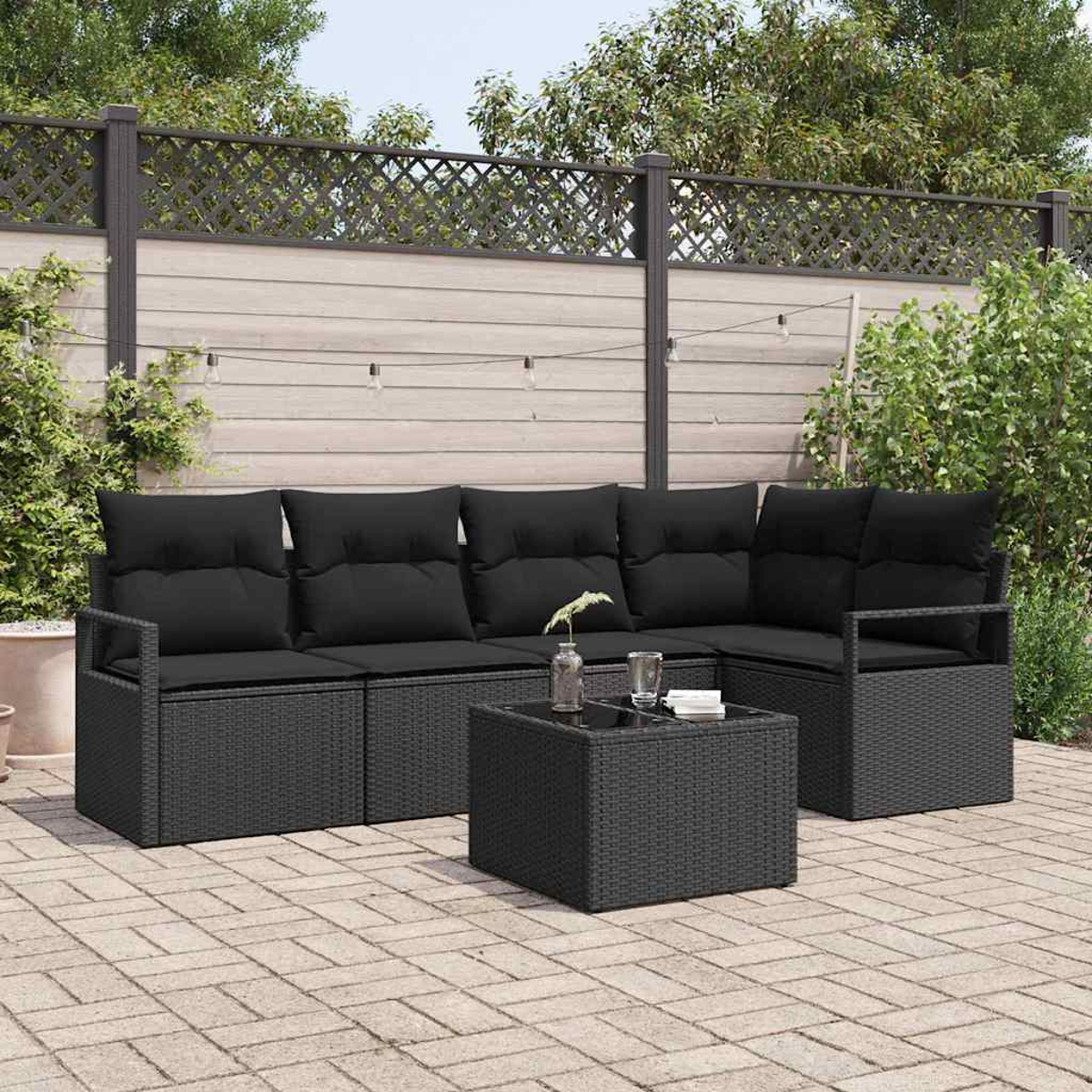 Schwarzes Outdoor-Ecksofa und Couchtisch aus Korbgeflecht. Dahinter ein Holzzaun und Pflanzen. Lichterketten hängen oben.