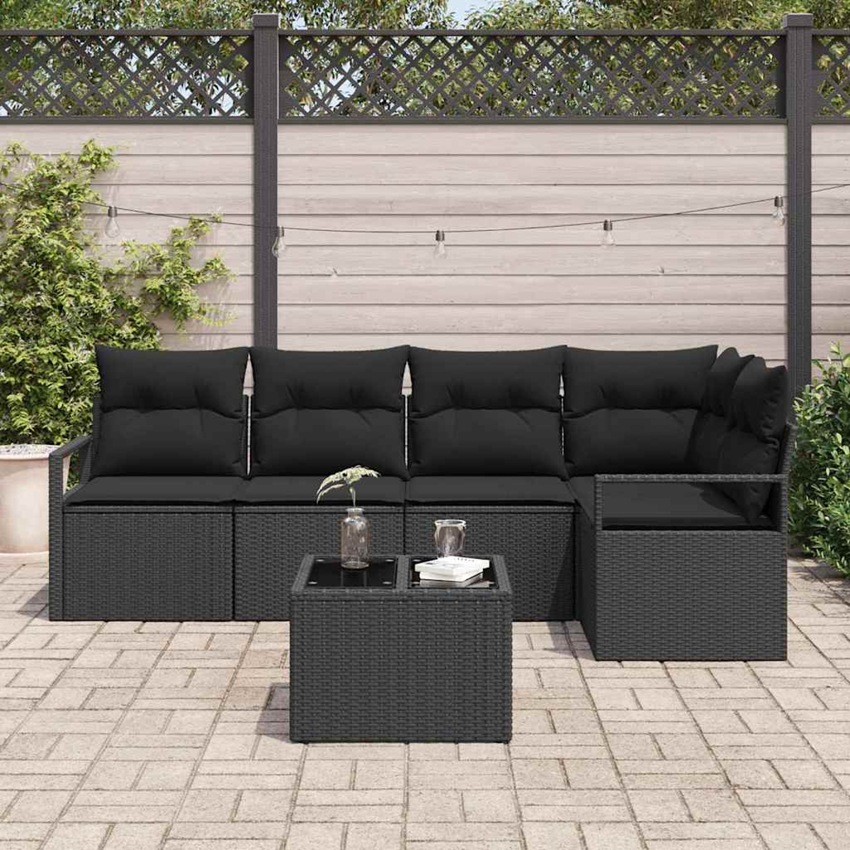 Schwarzes Outdoor-Ecksofa und kleiner Tisch auf der Terrasse. Im Hintergrund sind Zaun und Grün zu sehen.
