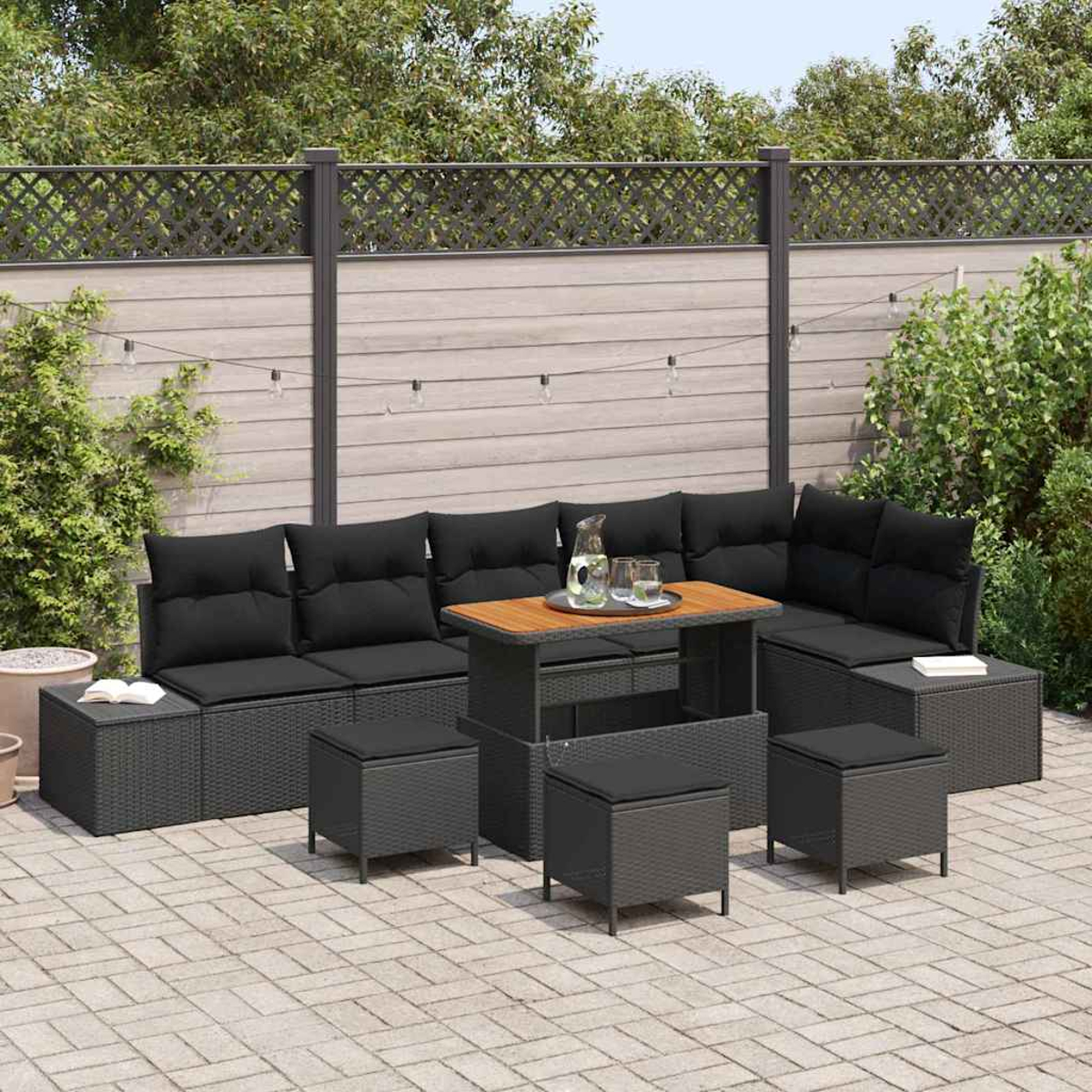 Garten-Terrassenset mit schwarzen Kissen, Holztisch und grauem Korbgeflecht. Das Set umfasst Sofa, Hocker und einen Tisch mit Glas und Wasserkrug.