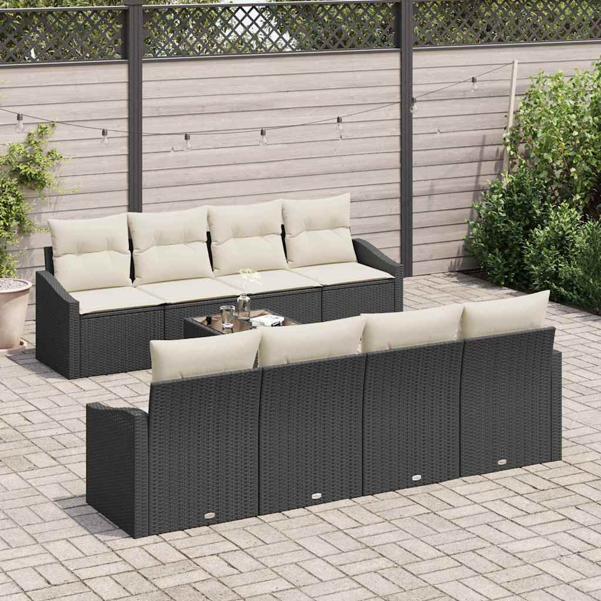 Terrassenset: dunkelgraue Korbsessel mit cremefarbenen Kissen, kleiner Glastisch, auf gepflasterter Terrasse. Umzäunter Hintergrund mit Pflanzen.