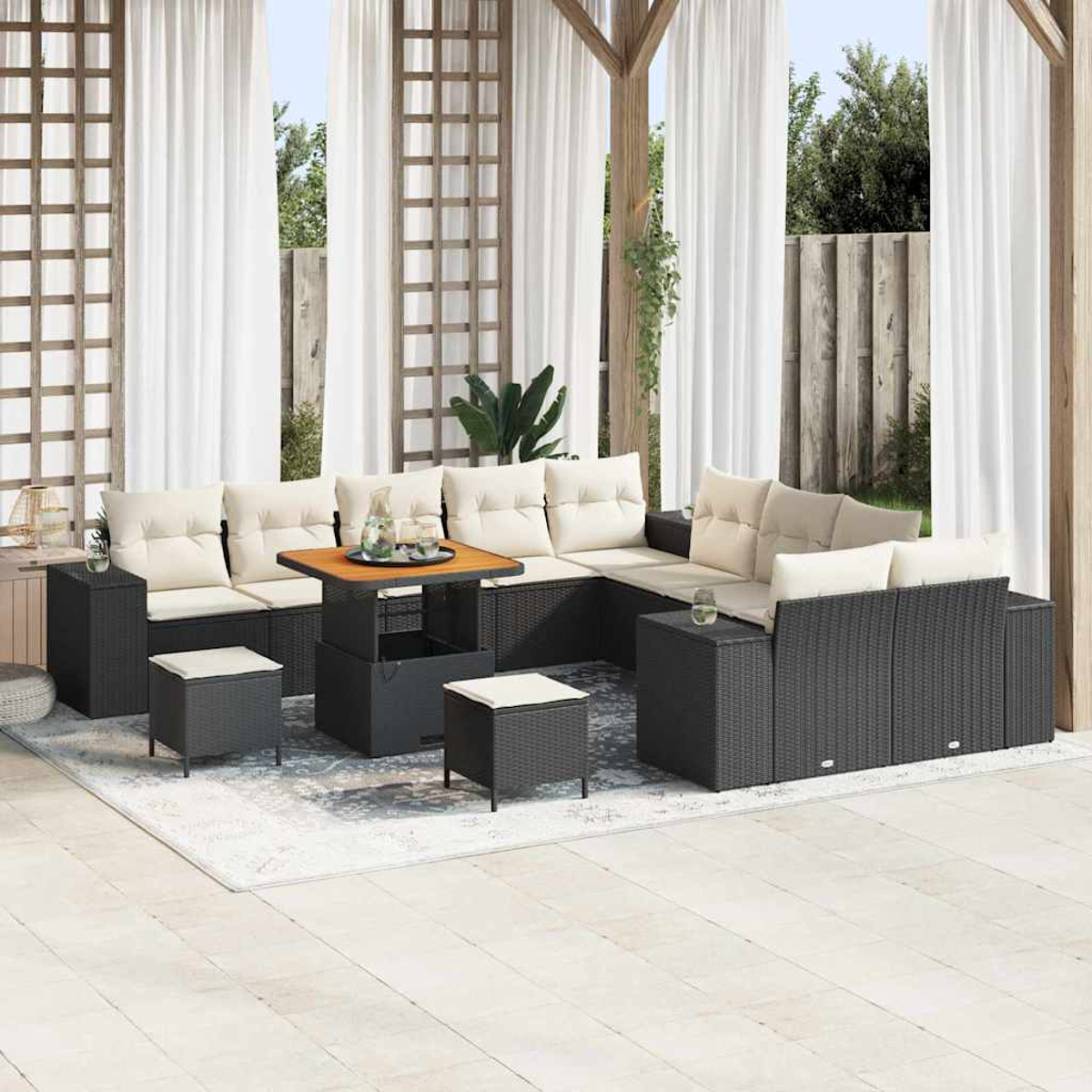 Terrassenmöbel-Set mit schwarzem Korbmöbel, cremefarbenen Kissen, Holztisch. Vorhänge und Garten im Hintergrund.