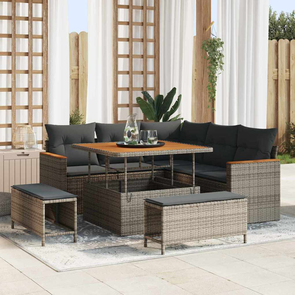 Terrassenset mit grauen Kissen, Holztisch und Korbmöbeln. Weiße Vorhänge und Holzzaun im Hintergrund.
