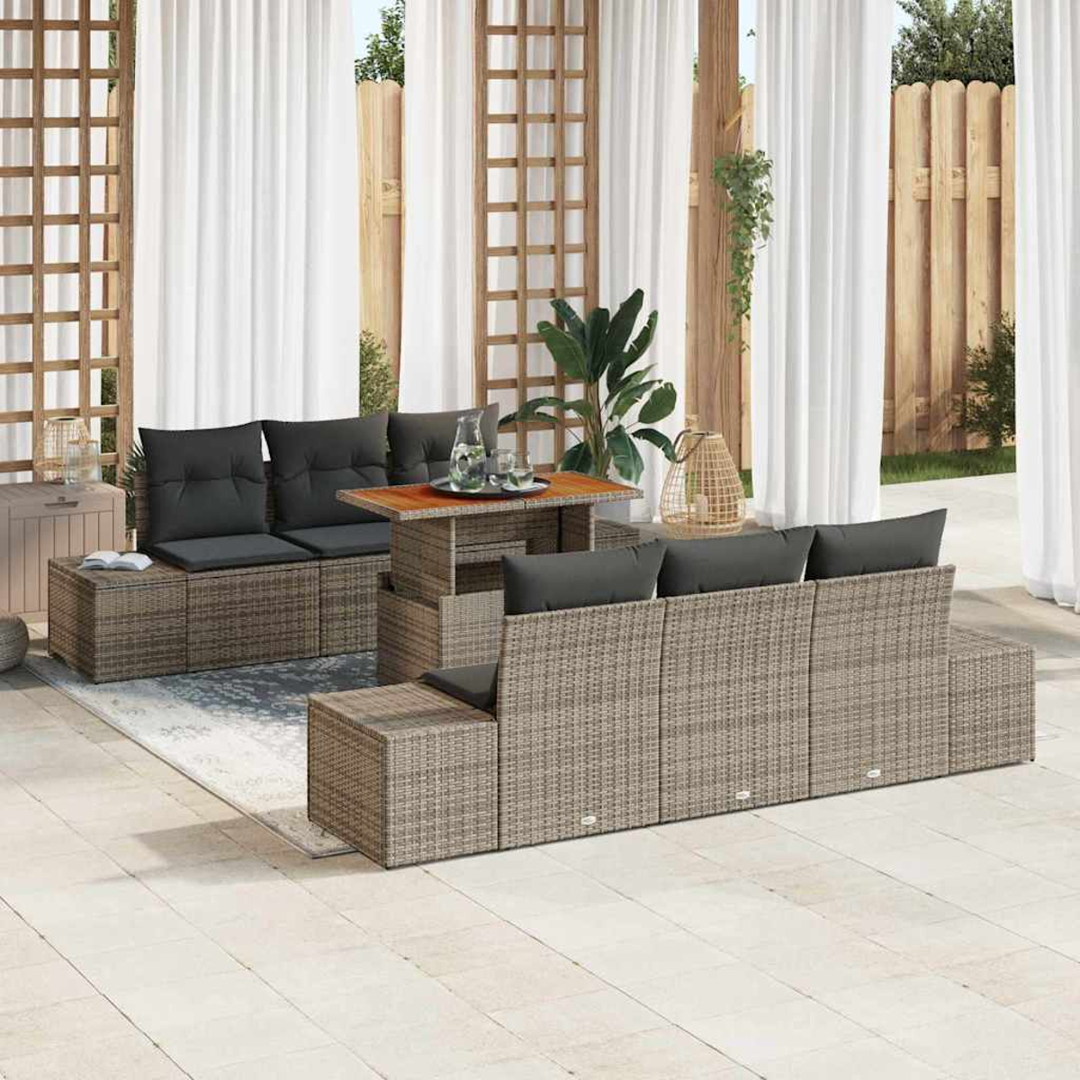 Outdoor-Rattan-Möbelset mit grauen Kissen. Enthält einen Tisch, Sofas und einen Beistelltisch. Weiße Vorhänge und Pflanzen im Hintergrund.