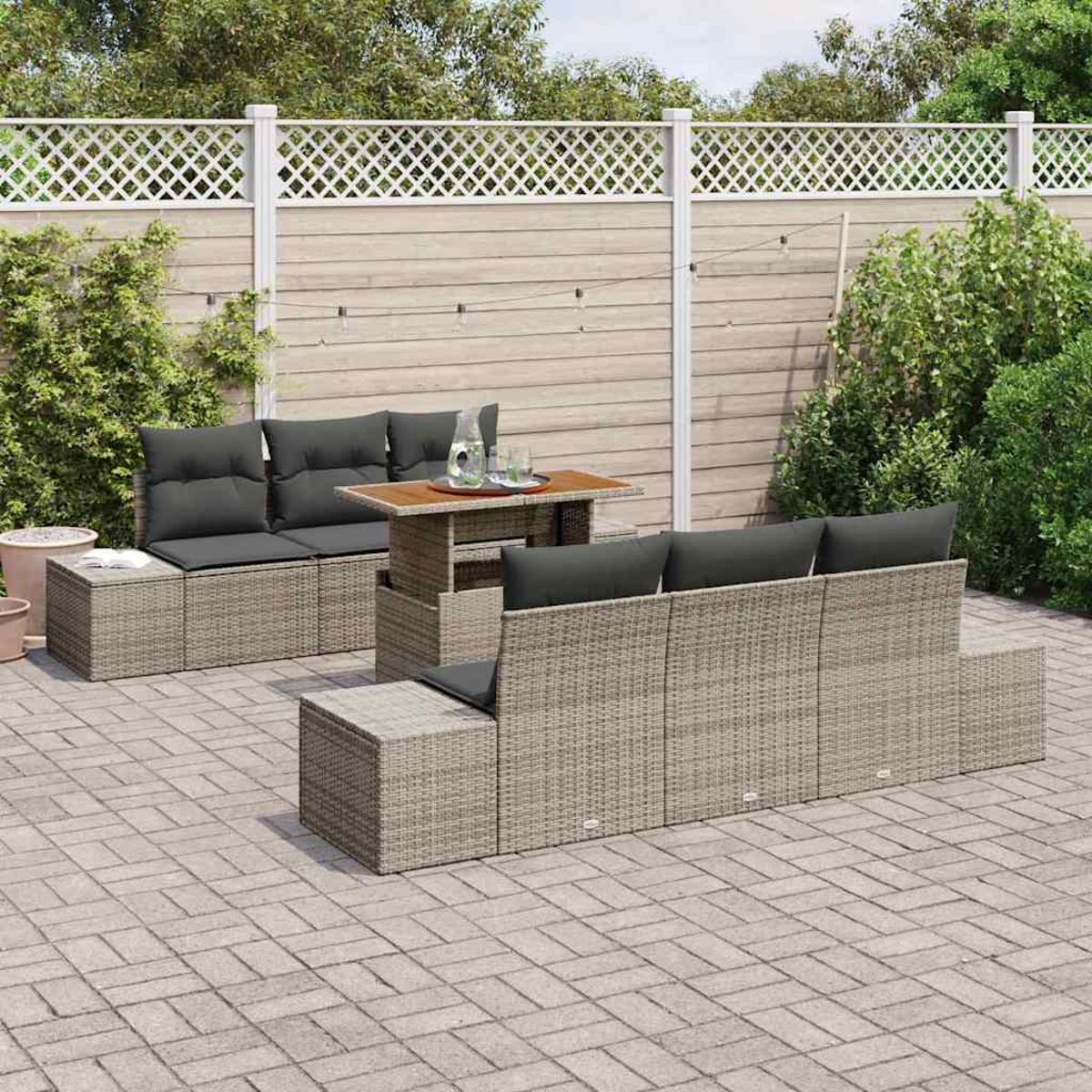 Gartenmöbel-Set für die Terrasse. Beinhaltet graue Korbsessel und Tisch mit Kissen. Der Hintergrund hat einen Holzzaun und Grün.