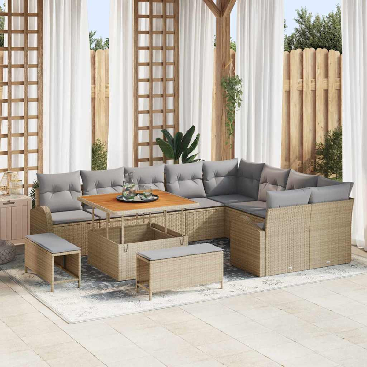 Outdoor-Sitzbereich mit Korbmöbeln, darunter ein Ecksofa, ein Couchtisch und Bänke. Graue Kissen und weiße Vorhänge im Hintergrund.