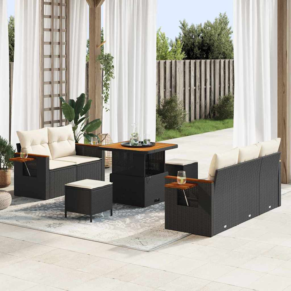 Juego de patio al aire libre con muebles de mimbre negro, cojines crema y una mesa cuadrada. Cortinas blancas y una valla de madera al fondo.
