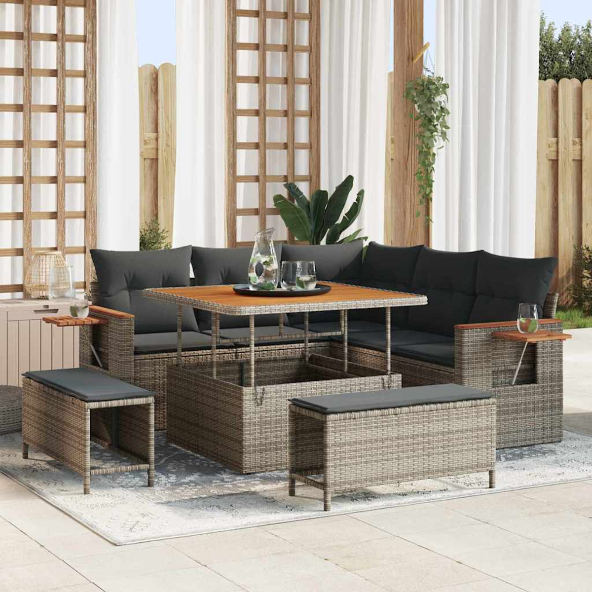 Outdoor-Rattan-Möbel-Set mit Tisch, Sofa und Ottomanen. Graue Kissen. Holzakzente. Weiße Vorhänge und Holzgitter im Hintergrund.