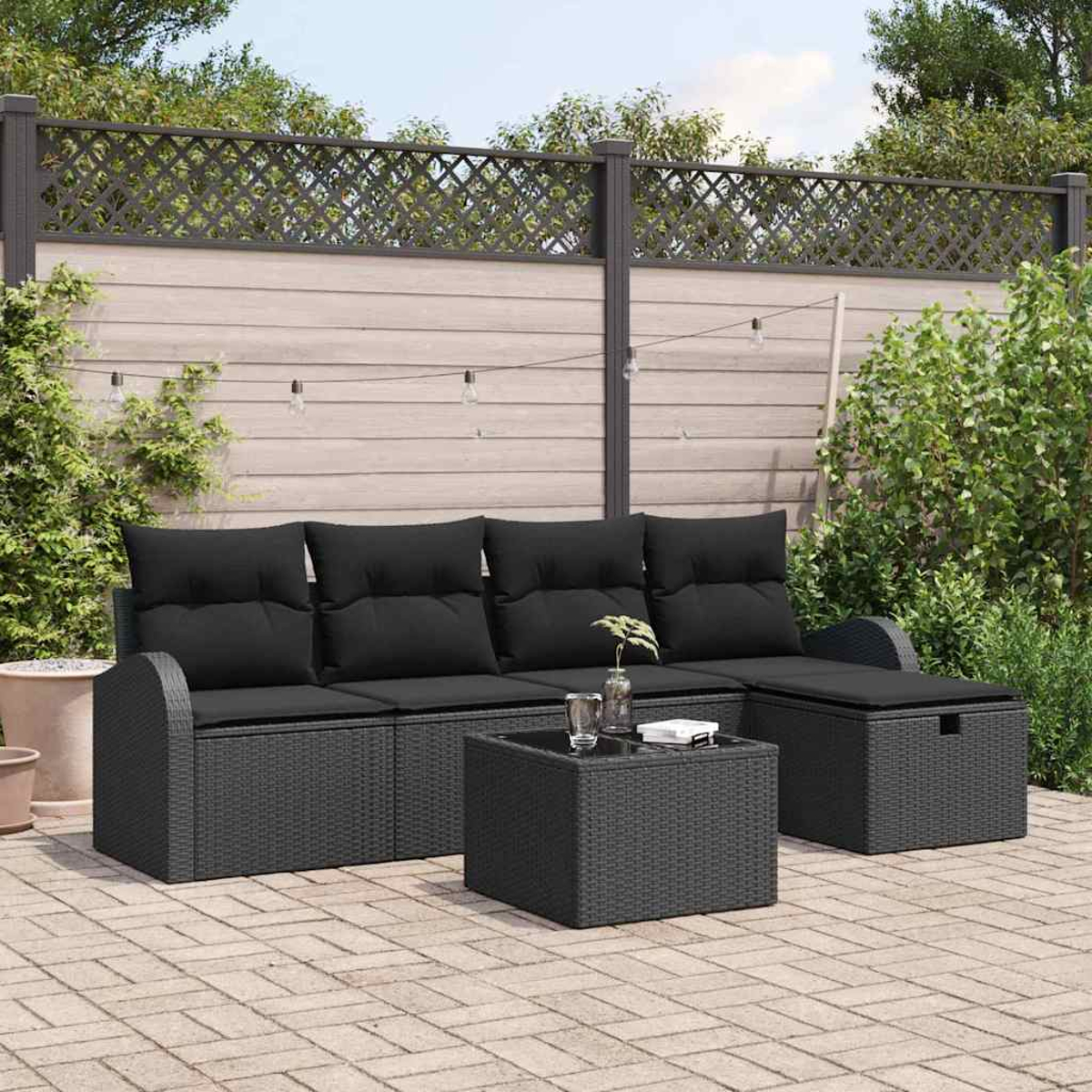 Gartenmöbel-Set. Schwarzes Korbmöbel-Sofa mit Kissen, Couchtisch und Stauraum-Hocker. Hintergrund mit Zaun und Pflanzen.