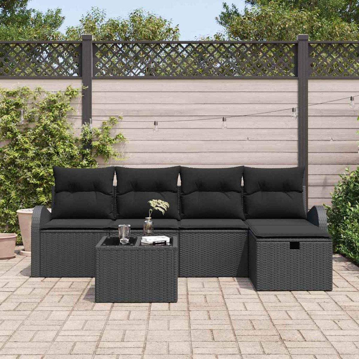 Terrassengarnitur: dunkelgraues Korbmöbel mit schwarzen Kissen, kleinem Tisch und Stauraum vor Holzzaun.