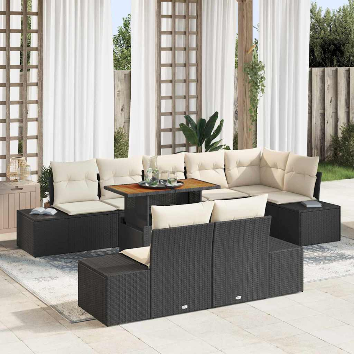 Garten-Sitzgruppe: schwarze Korbsessel mit cremefarbenen Kissen, Holztisch mit Getränken, weiße Vorhänge und ein Holzgitter.