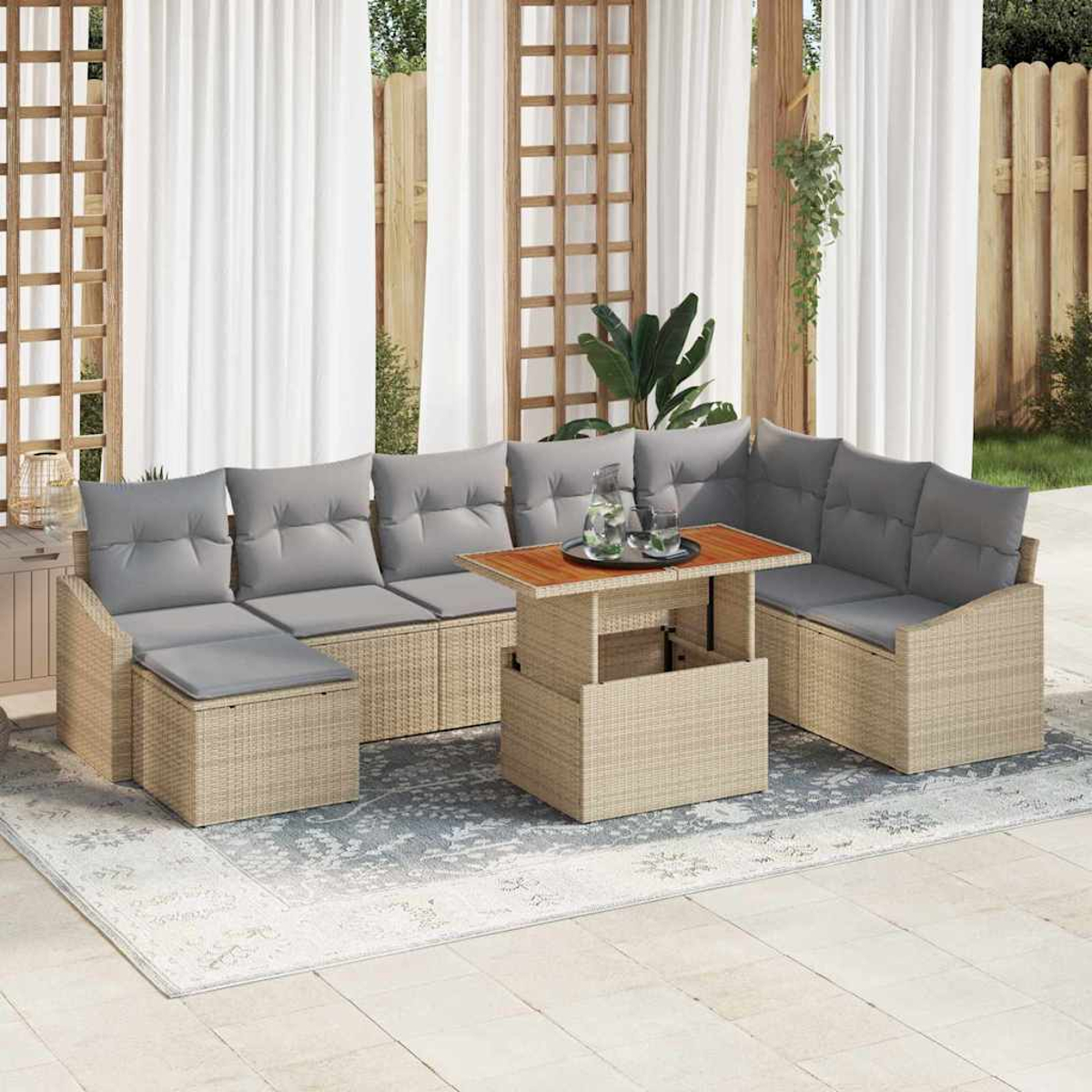 Outdoor-Rattan-Sofagarnitur mit grauen Kissen und einem Holztisch. Weiße Vorhänge und ein Zaun im Hintergrund. Getränke stehen auf dem Tisch.