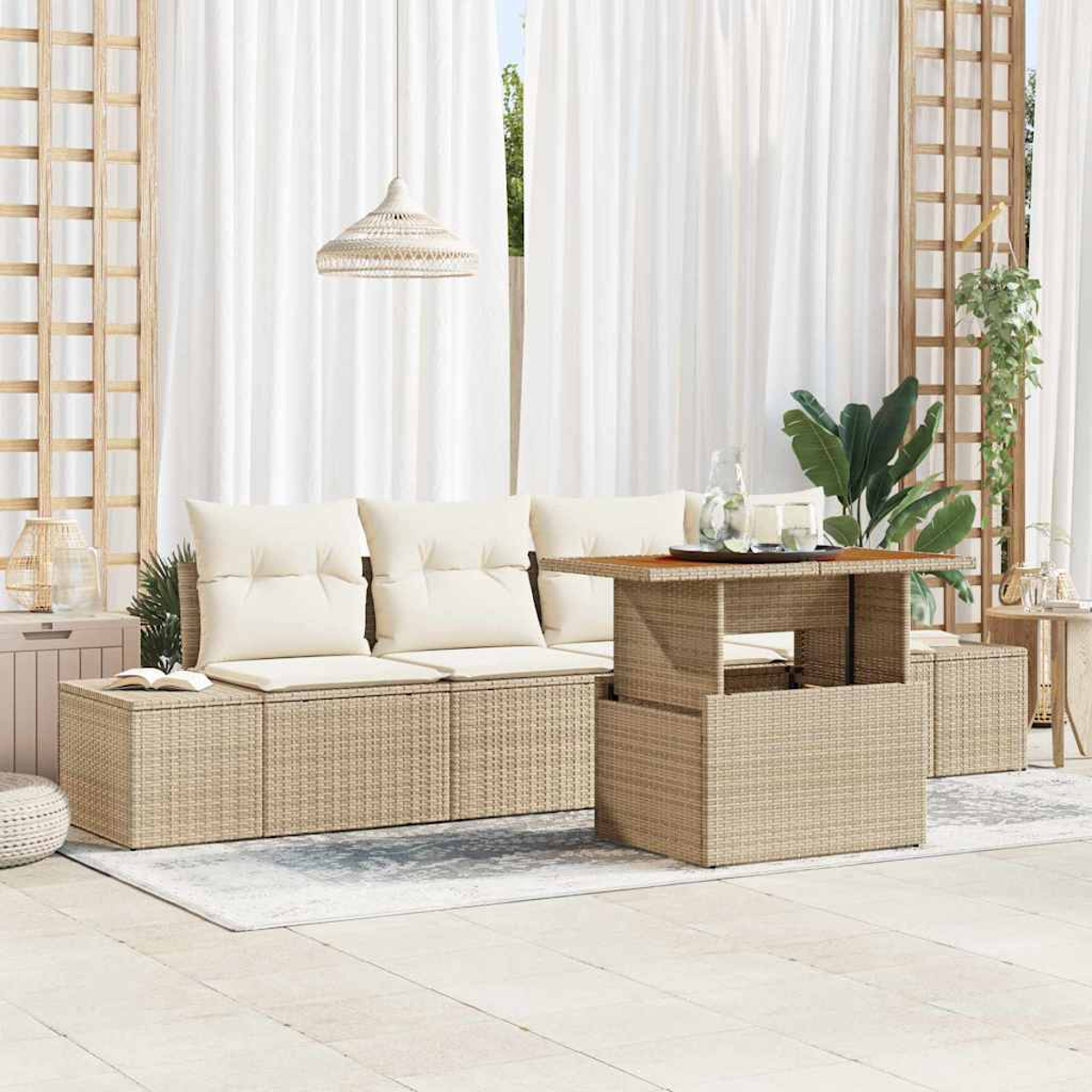 Außenbereich mit beigen Rattanmöbeln, Kissen und einem Tisch. Weiße Vorhänge und Pflanzen im Hintergrund.