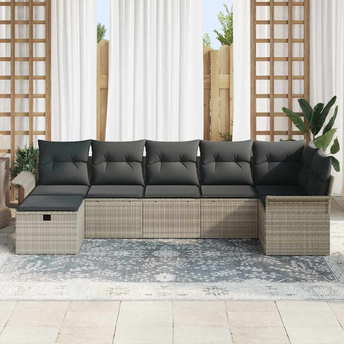 Outdoor-Ecksofa mit grauen Kissen auf einem gemusterten Teppich. Weiße Vorhänge und Holzgitter im Hintergrund.
