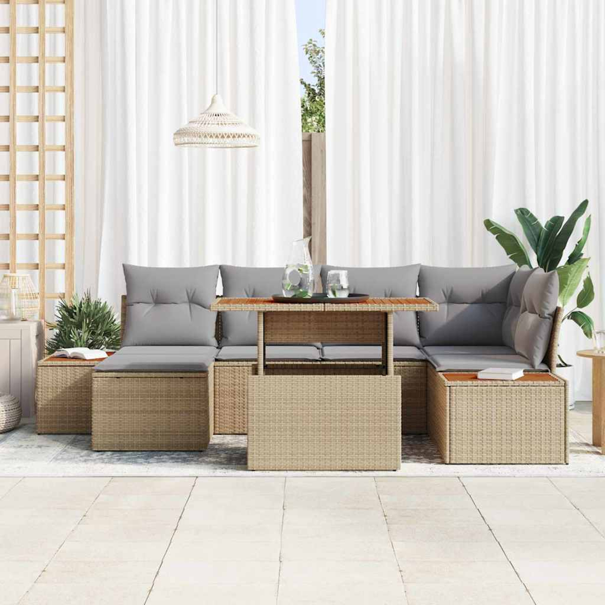 Gartenmöbel-Set aus Korbgeflecht mit grauen Kissen. Ein Tisch trägt Wasserkrug und Gläser. Weiße Vorhänge und Pflanzen im Hintergrund.