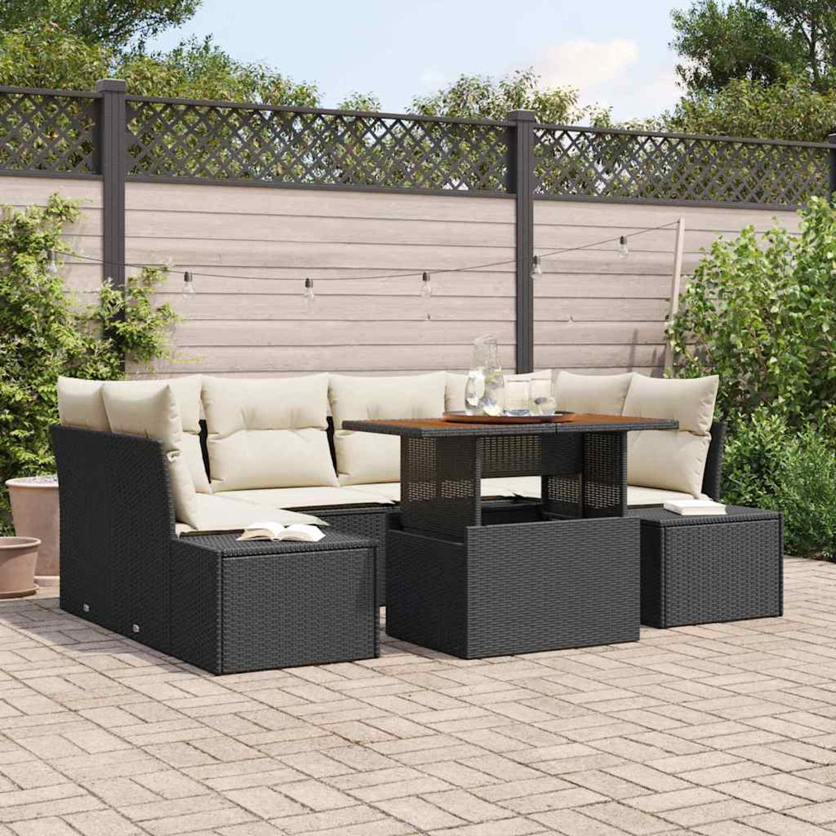 Garten-Sitzgruppe mit schwarzem Korbmöbel, beigefarbenen Kissen und einem Tisch mit Hubfunktion. Ziegelpflasterung im Vordergrund und Zaun im Hintergrund.