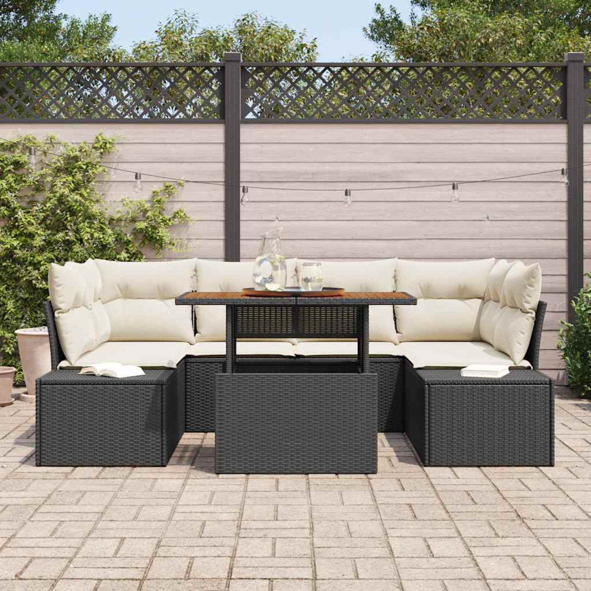 Outdoor-Ecksofa mit beigefarbenen Kissen, schwarzem Korbgewebe und einem Holztisch. Im Hintergrund ein Zaun und Grün.