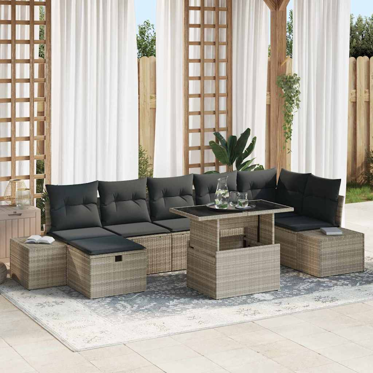 Juego de asientos al aire libre con cojines grises y una mesa sobre una alfombra estampada. Cortinas blancas y estructura de madera.