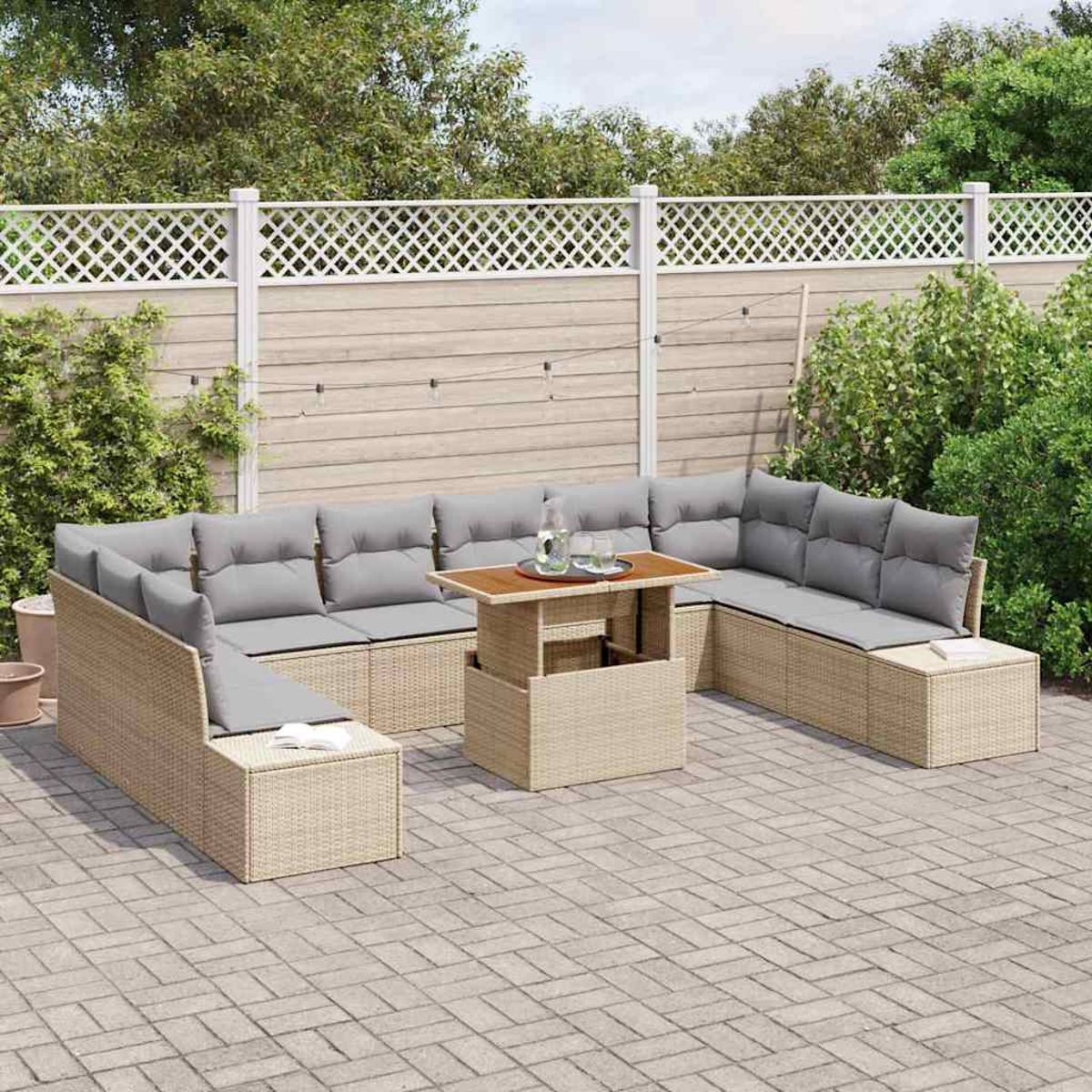 Garten-Sitzgruppe mit grauen Kissen und Tisch. Beige Rattanmöbel auf einer Ziegelterrasse, mit weißem Zaun und Grün im Hintergrund.