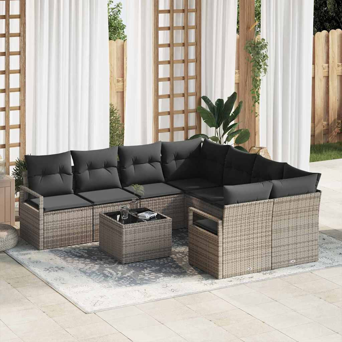Outdoor-Ecksofa mit dunkelgrauen Kissen. Ein kleiner Tisch steht auf einem Teppich. Weiße Vorhänge und ein Holzzaun sind im Hintergrund zu sehen.