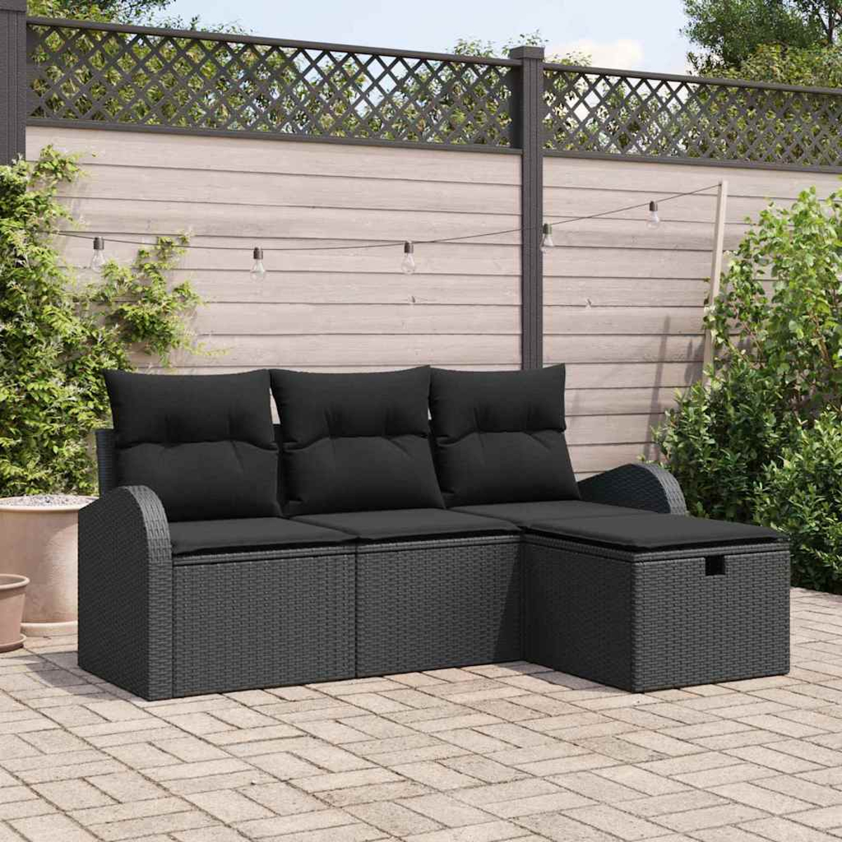 Ein dunkelgraues Korbsessel-Sofa mit schwarzen Kissen steht auf einer Terrasse. Im Hintergrund ein Holzzaun und Pflanzen.