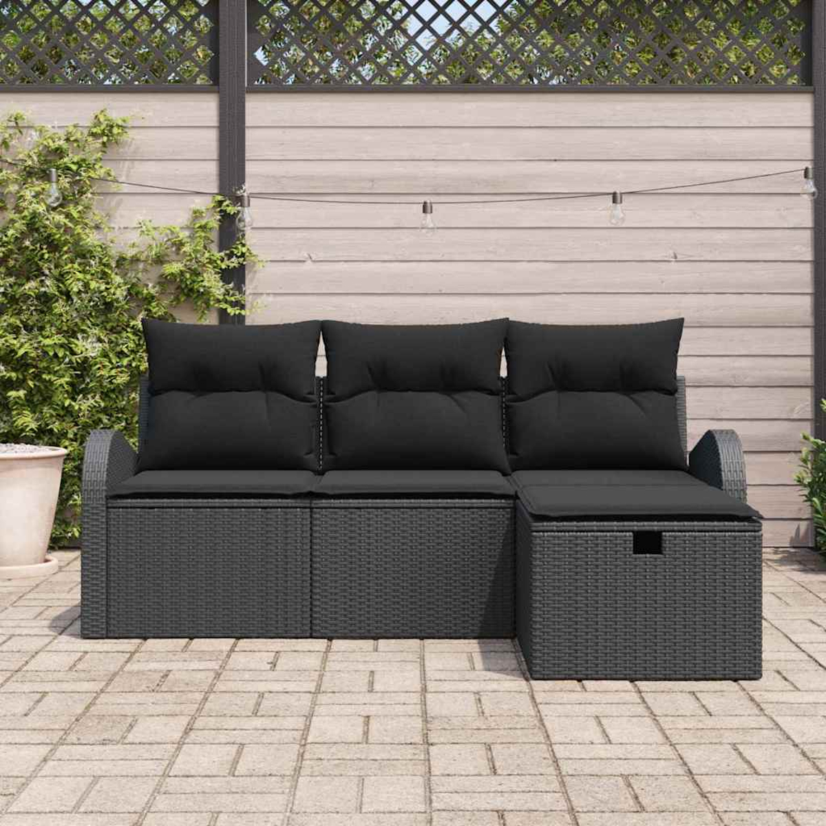 Gartensofa mit schwarzen Kissen. Auf einer Backsteinterrasse, vor Holzzaun und Kletterpflanze.