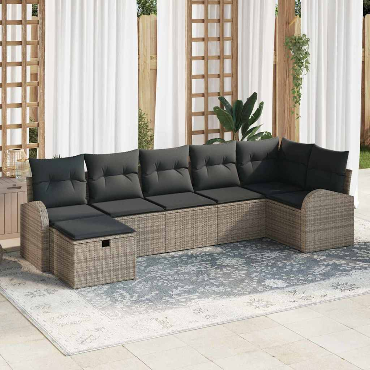 Ein Ecksofa im Freien mit grauen Kissen und gewebter Basis steht auf einem Teppich. Weiße Vorhänge und hölzerner Spalier im Hintergrund.