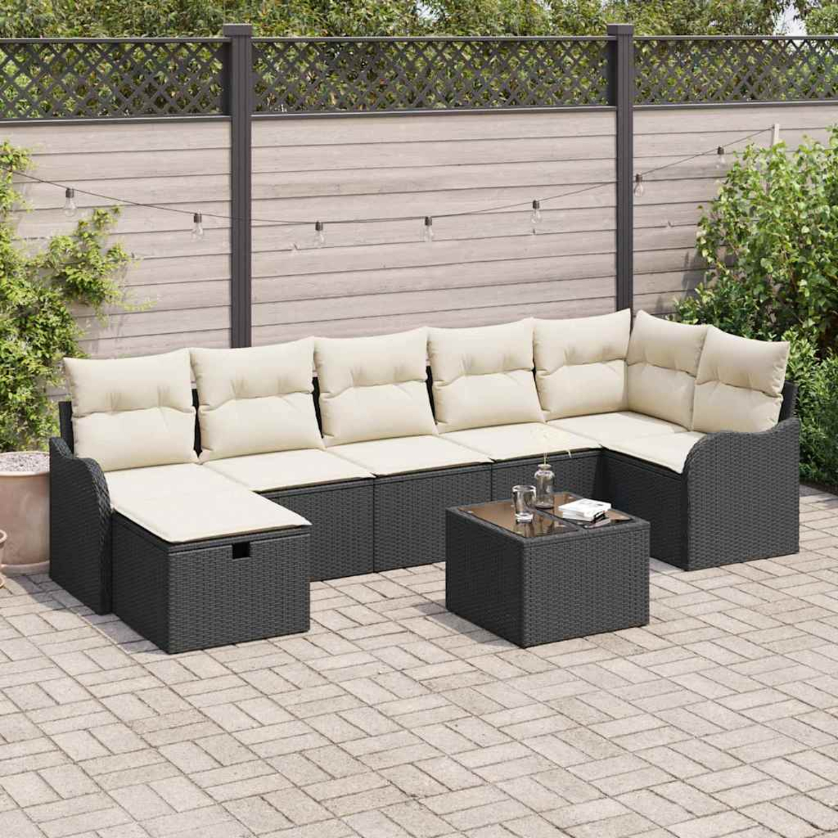 Outdoor-Ecksofa mit cremefarbenen Kissen und einem kleinen Tisch mit Gläsern. Dahinter sind ein Holzzaun und Pflanzen.