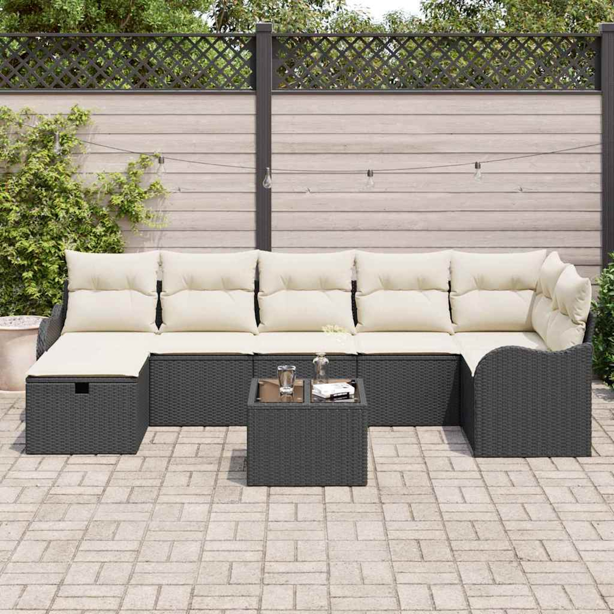 Outdoor-Ecksofa mit cremefarbenen Kissen und einem kleinen Tisch auf einer Ziegelterrasse. Hintergrund ist ein Zaun und Grün.