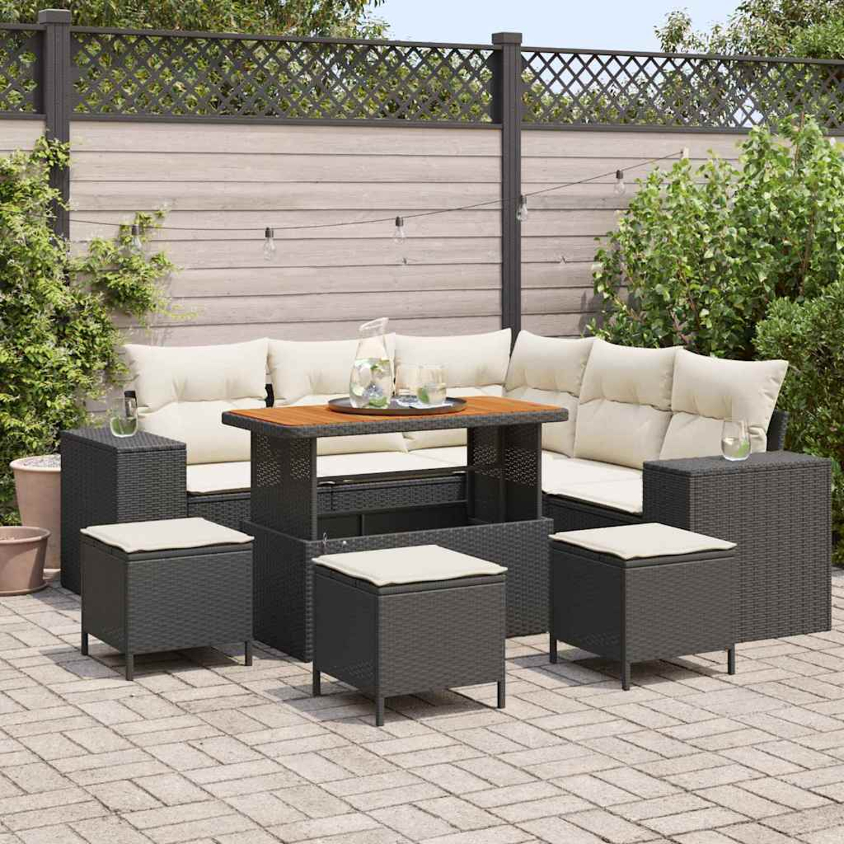 Set da patio esterno con tavolo, divano e sgabelli su un patio in mattoni. Lo sfondo ha una recinzione in legno e vegetazione.