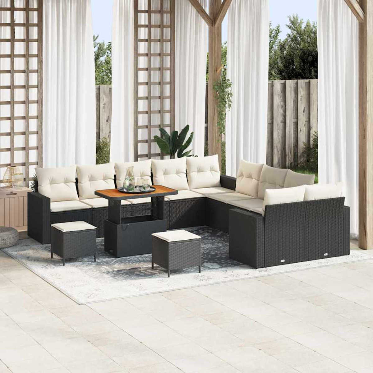 Terrassenset mit schwarzem Korbsessel, cremefarbenen Kissen, Holztisch und kleinen Hockern auf einem Teppich, Vorhängen und Grün im Hintergrund.