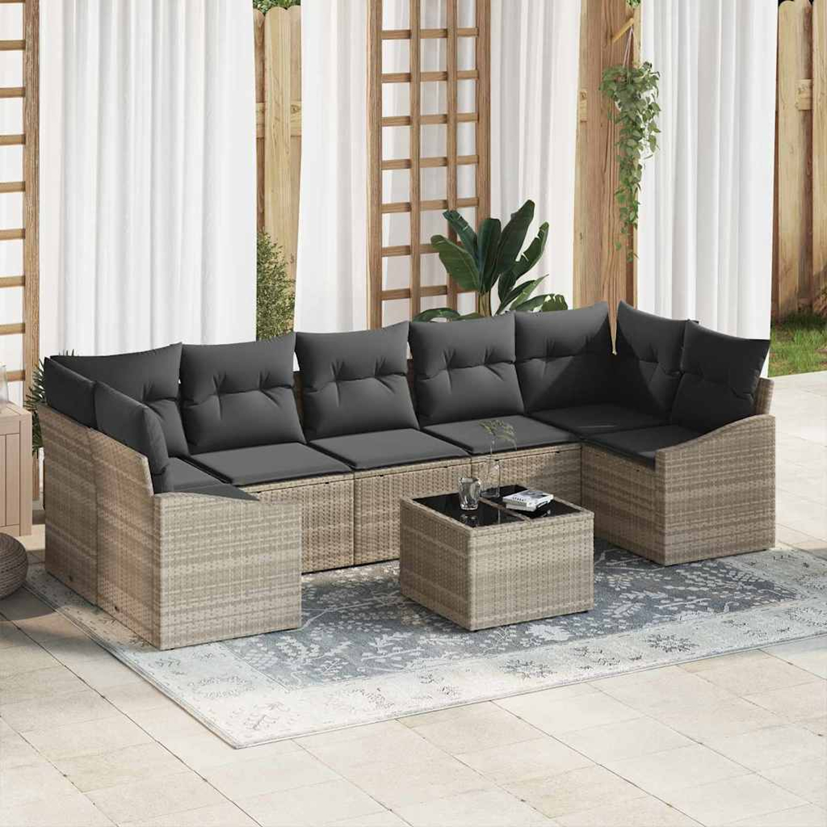 Ein Sitzbereich im Freien mit einem Ecksofa und einem Couchtisch auf einem gemusterten Teppich. Graue Kissen stehen im Kontrast zu dem hellbraunen Korbgeflecht.
