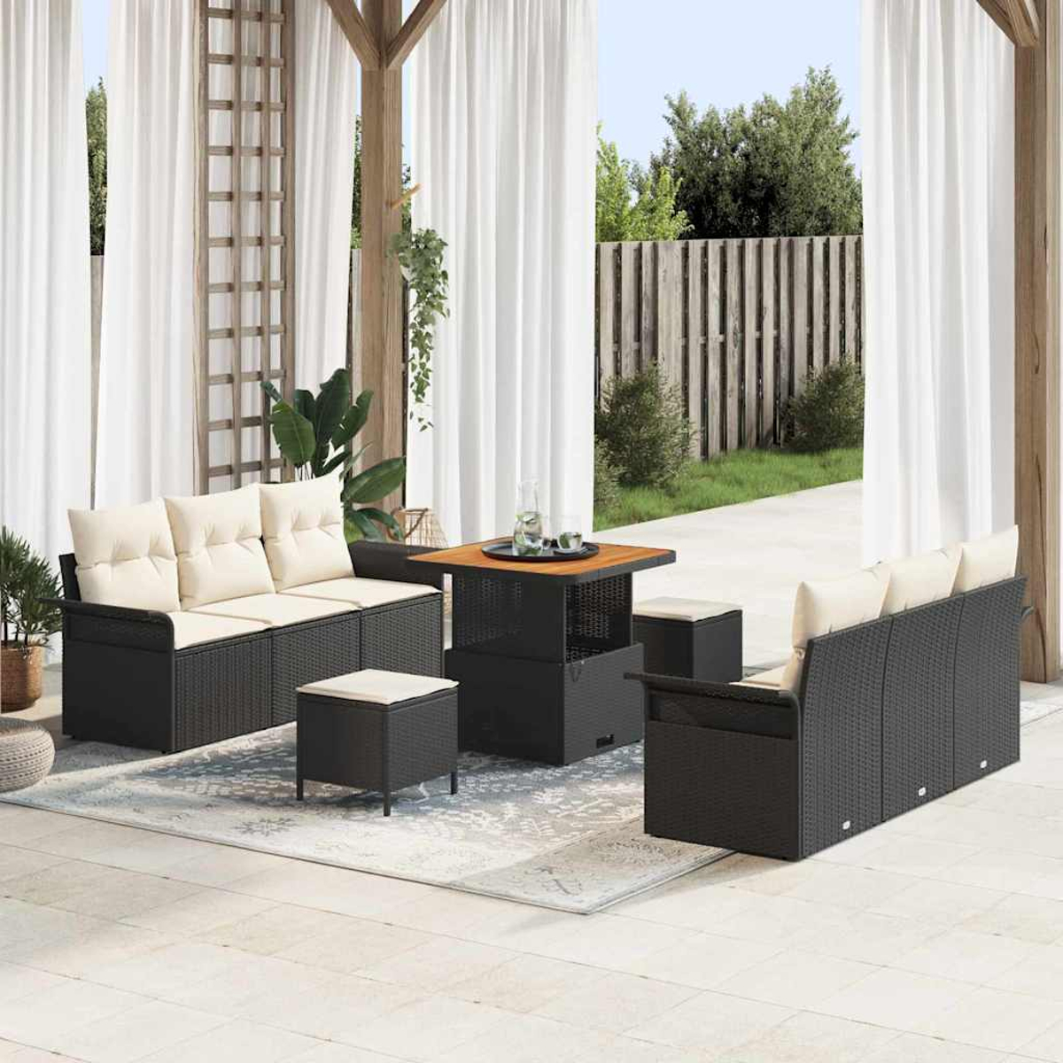 Gartenmöbel-Set mit schwarzen, gewebten Rahmen, cremefarbenen Kissen und einem Holztisch. Weiße Vorhänge und ein Holzzaun im Hintergrund.