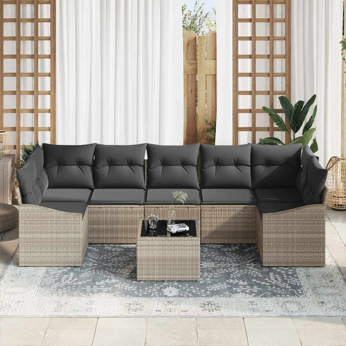 Ein Outdoor-Ecksofa mit grauen Kissen und einem kleinen Tisch. Es steht auf einem gemusterten Teppich, in der Nähe von weißen Vorhängen und Holzrahmen.