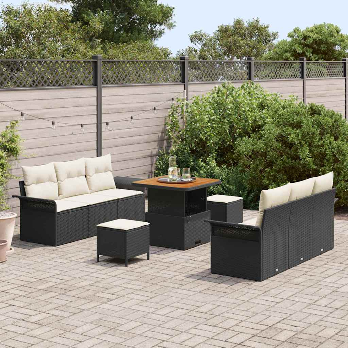Terrassenmöbel-Set mit schwarzer Korbmöbeln, cremefarbenen Kissen und einem Holztisch. Ein Zaun und üppiges Grün vervollständigen die Szene.