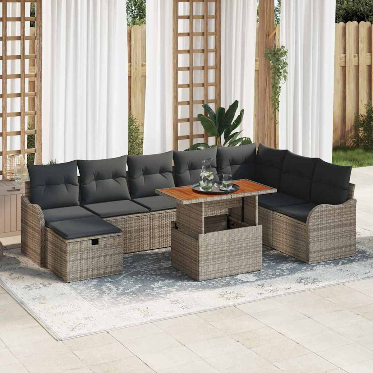 Outdoor-Ecksofa mit grauen Kissen, einem Holztisch mit Getränken und einem Teppich, vor weißen Vorhängen und einem Holzzaun.