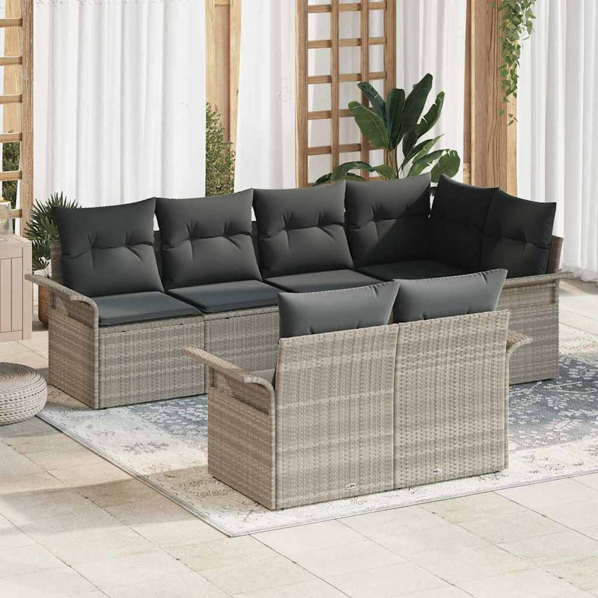 Geflochtene Gartenmöbel mit grauen Kissen. Beinhaltet ein Sofa und zwei Stühle auf einem gemusterten Teppich vor weißem Vorhang.