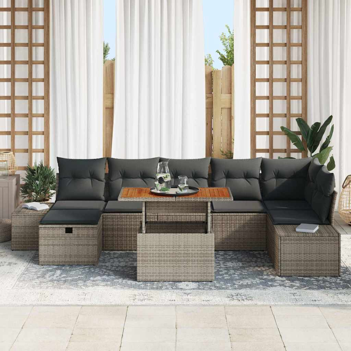 Sofá seccional exterior con cojines grises y mesa de madera, bebidas, cortinas y plantas en el fondo, sobre una alfombra.