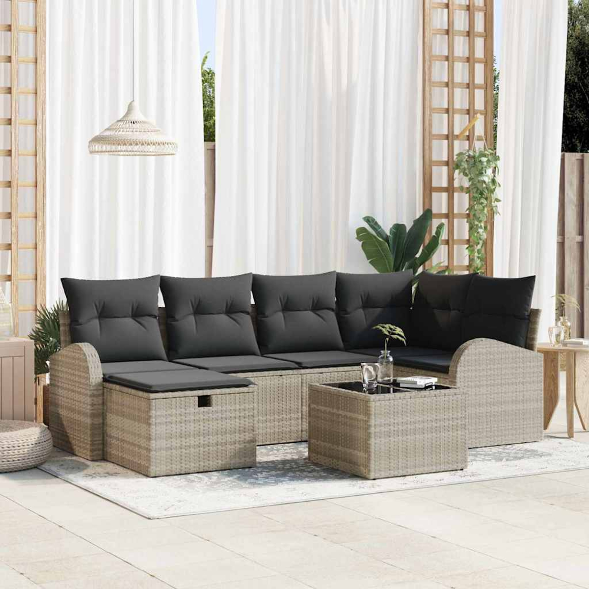 Gartenmöbel-Set. Graue Kissen auf hellbraunem Korbgeflecht, kleiner Tisch, weiße Vorhänge und eine Hängelampe.