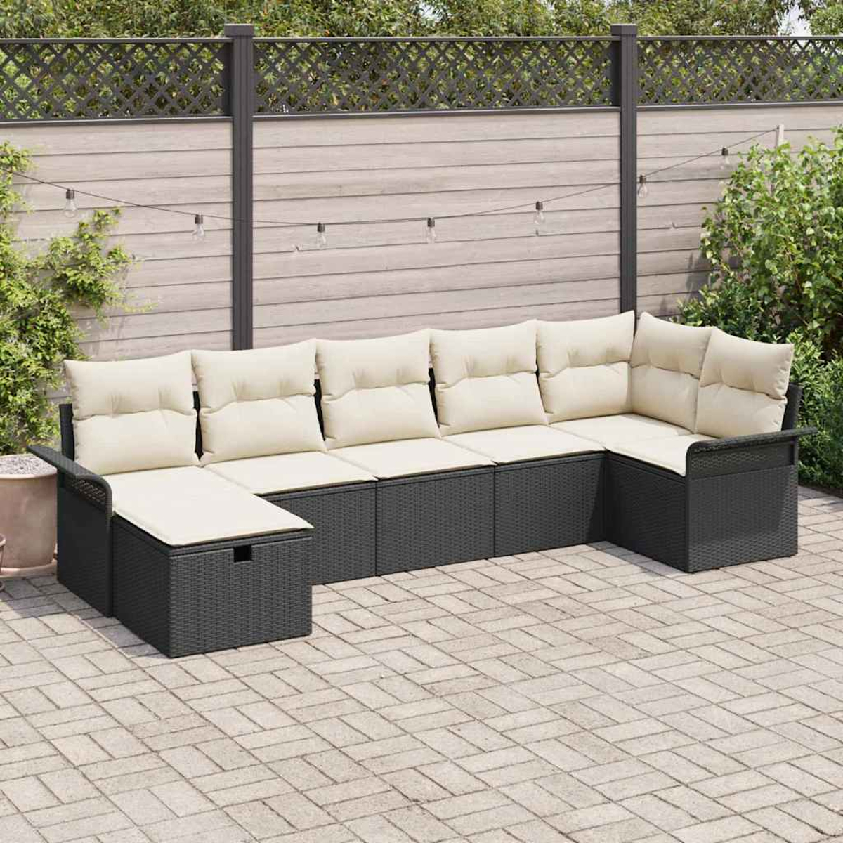U-förmiges Outdoor-Ecksofa mit cremefarbenen Kissen auf grauem Korbgeflechtrahmen, auf einer Ziegelterrasse, Zaun im Hintergrund.
