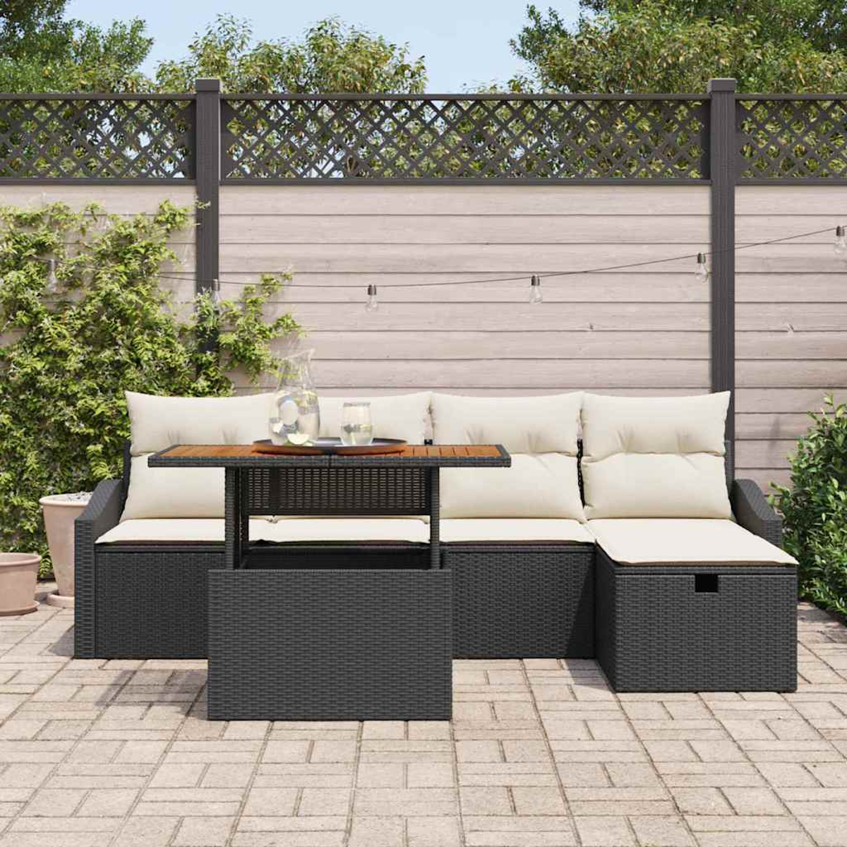 Sitzbereich im Freien mit einem grauen Rattan-Sofa, beigen Kissen und einem Holztisch auf einer Steinterrasse.