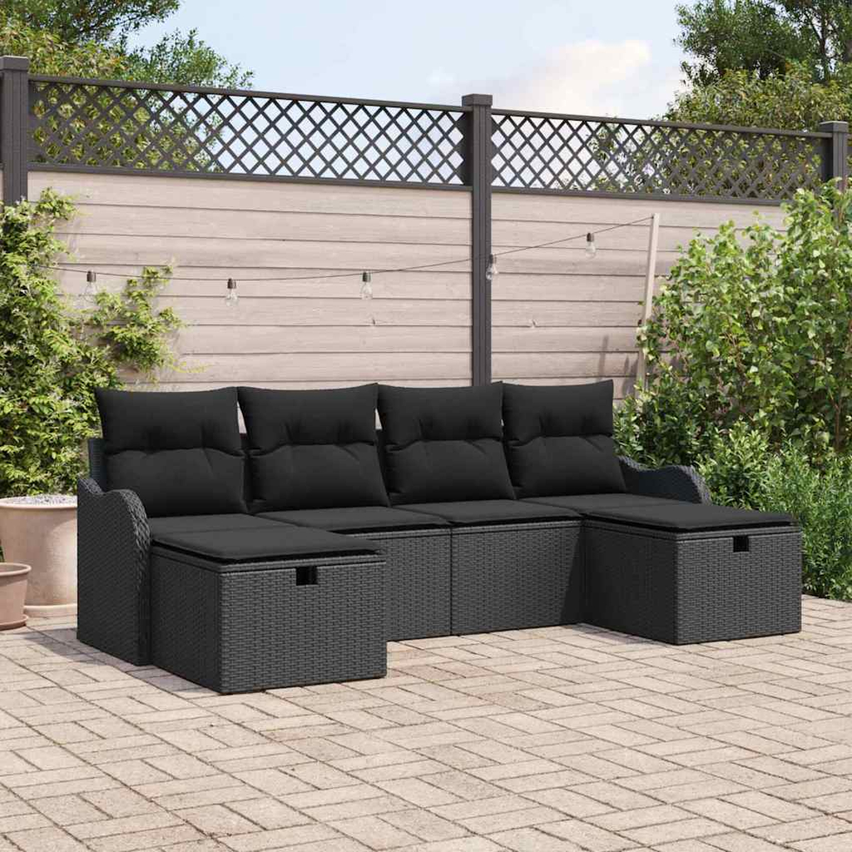 Ein schwarzes Outdoor-Sofa aus Korbgeflecht mit schwarzen Kissen steht auf einer Ziegelstein-Terrasse. Im Hintergrund sind ein Zaun und Pflanzen zu sehen.