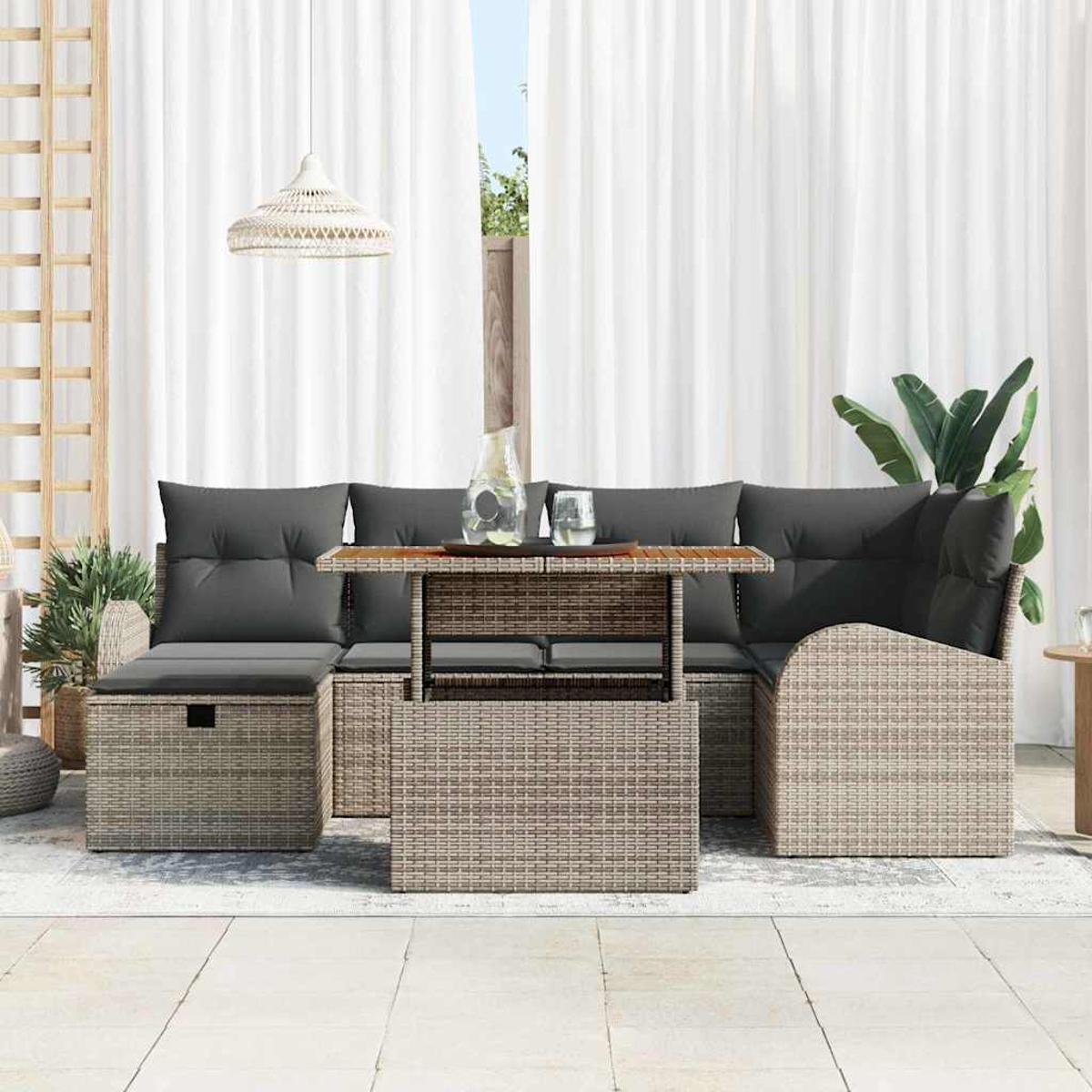 Outdoor-Korbmöbelset mit grauen Kissen und einem Couchtisch mit Hubtisch. Weiße Vorhänge und Pflanzen im Hintergrund.