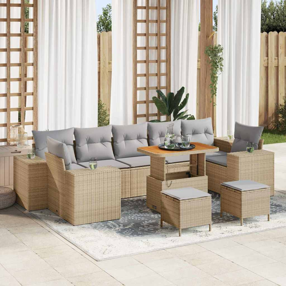 Juego de patio: sofá de mimbre beige, sillones y otomanas con cojines grises, mesa de madera y cortinas blancas.