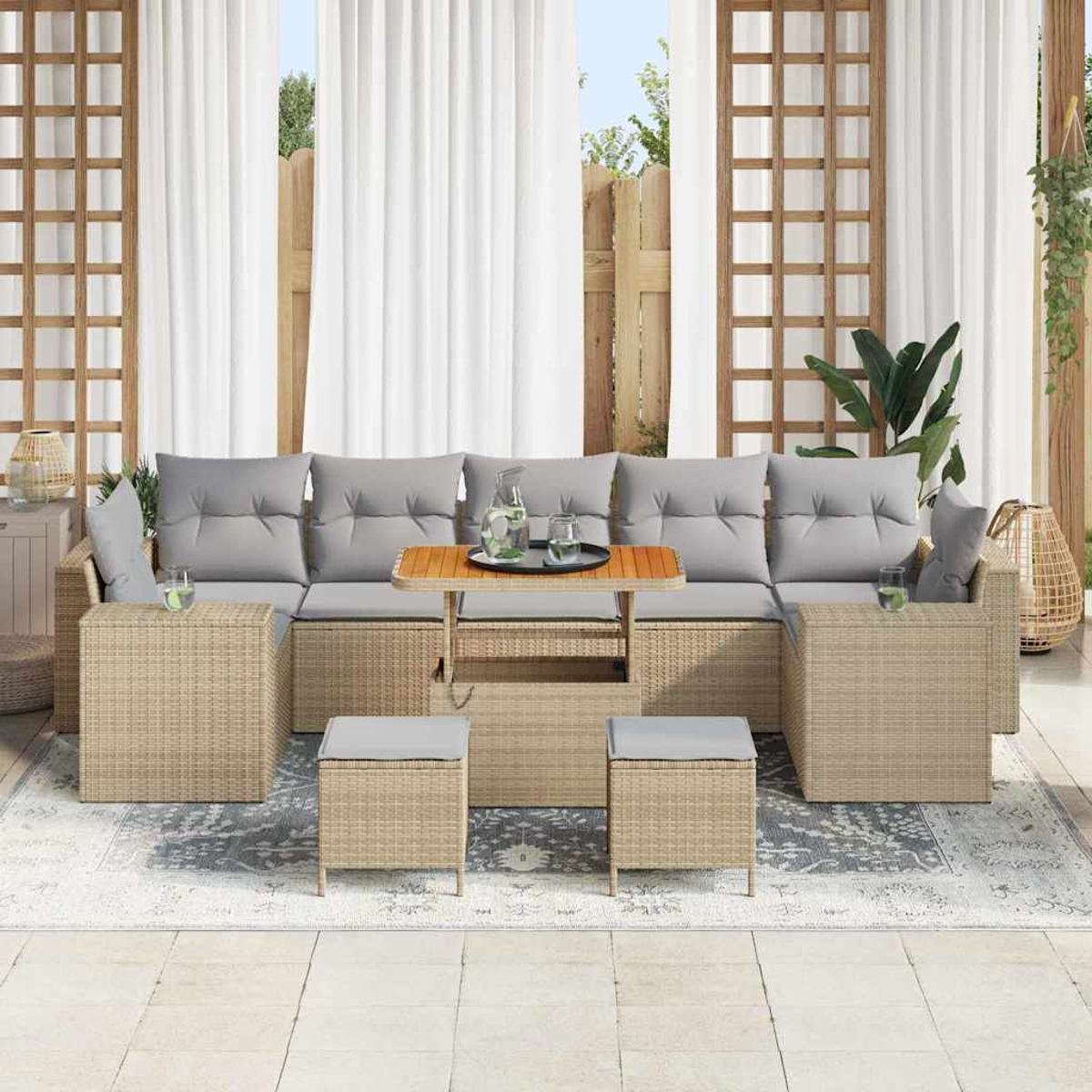 Un juego de patio al aire libre con un sofá grande, mesas auxiliares, otomanas y una mesa de centro. Cojines grises, cortinas blancas y alfombra.