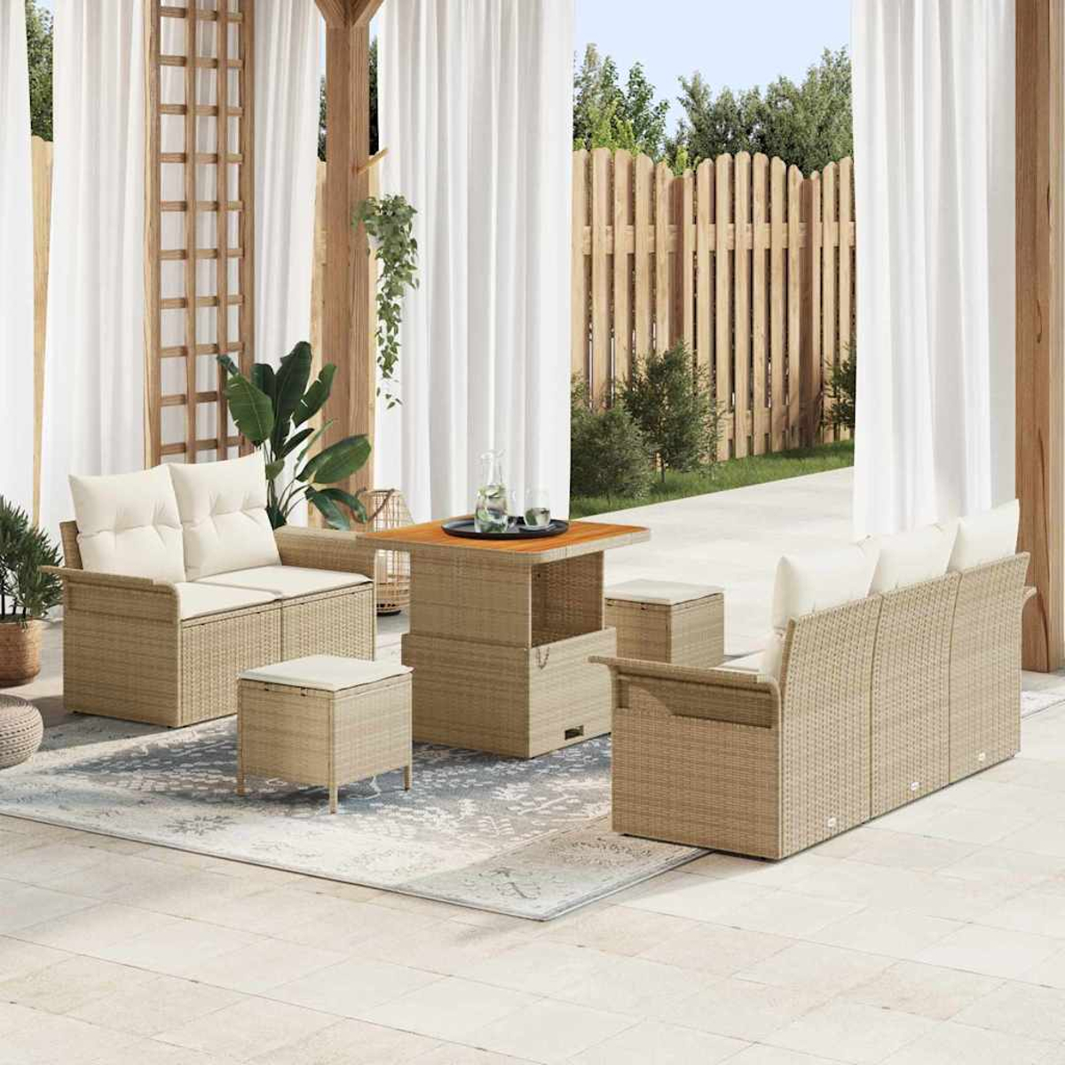 Gartenmöbel-Set aus Korbgeflecht mit Tisch, Loveseat, Sofa und Hockern auf einer Terrasse mit weißen Vorhängen und Holzzaun.