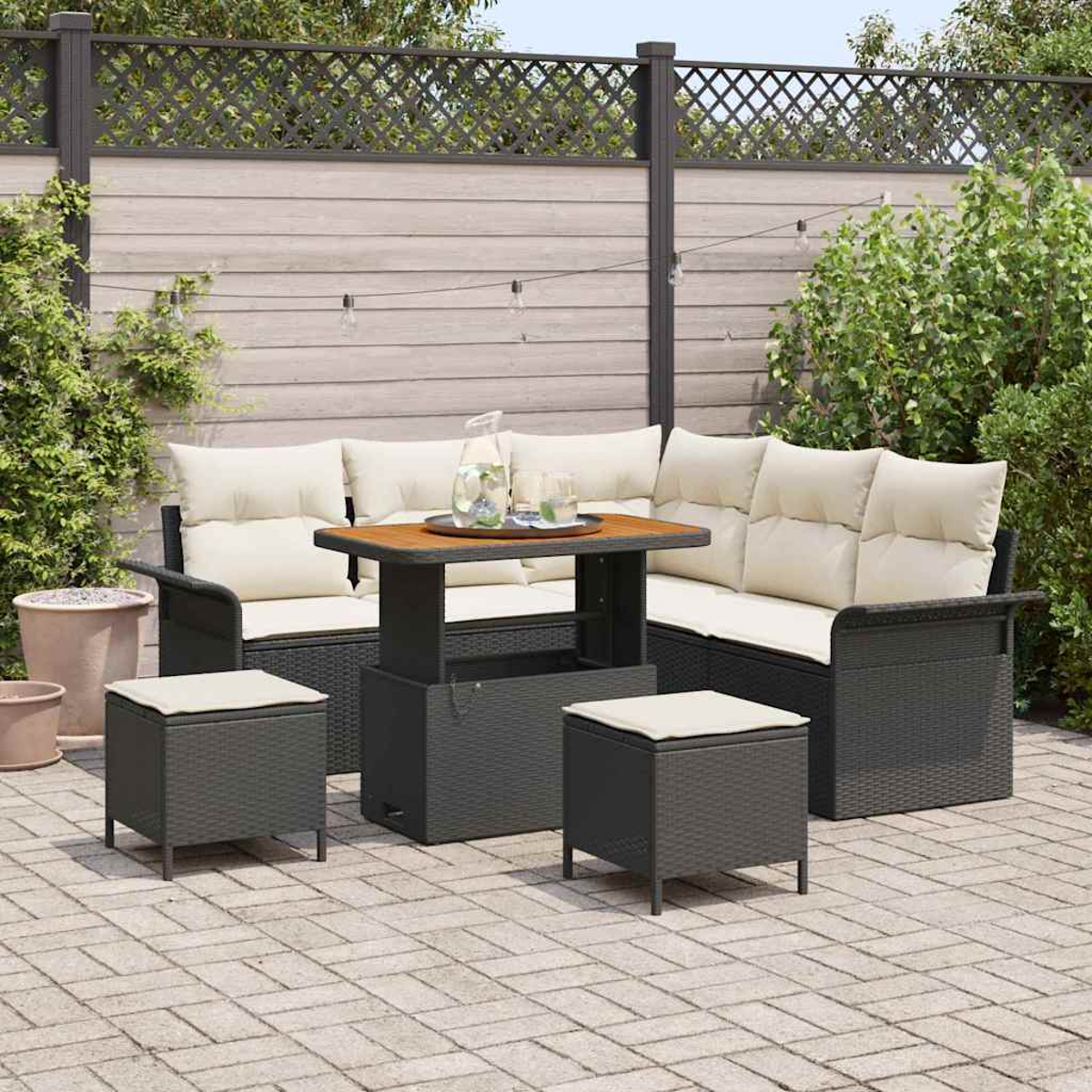 Garten-Terrassenset mit dunkelgrauen Korbmöbeln, cremefarbenen Kissen und einem Holztisch. Auf einer Backstein-Terrasse, umgeben von Pflanzen.