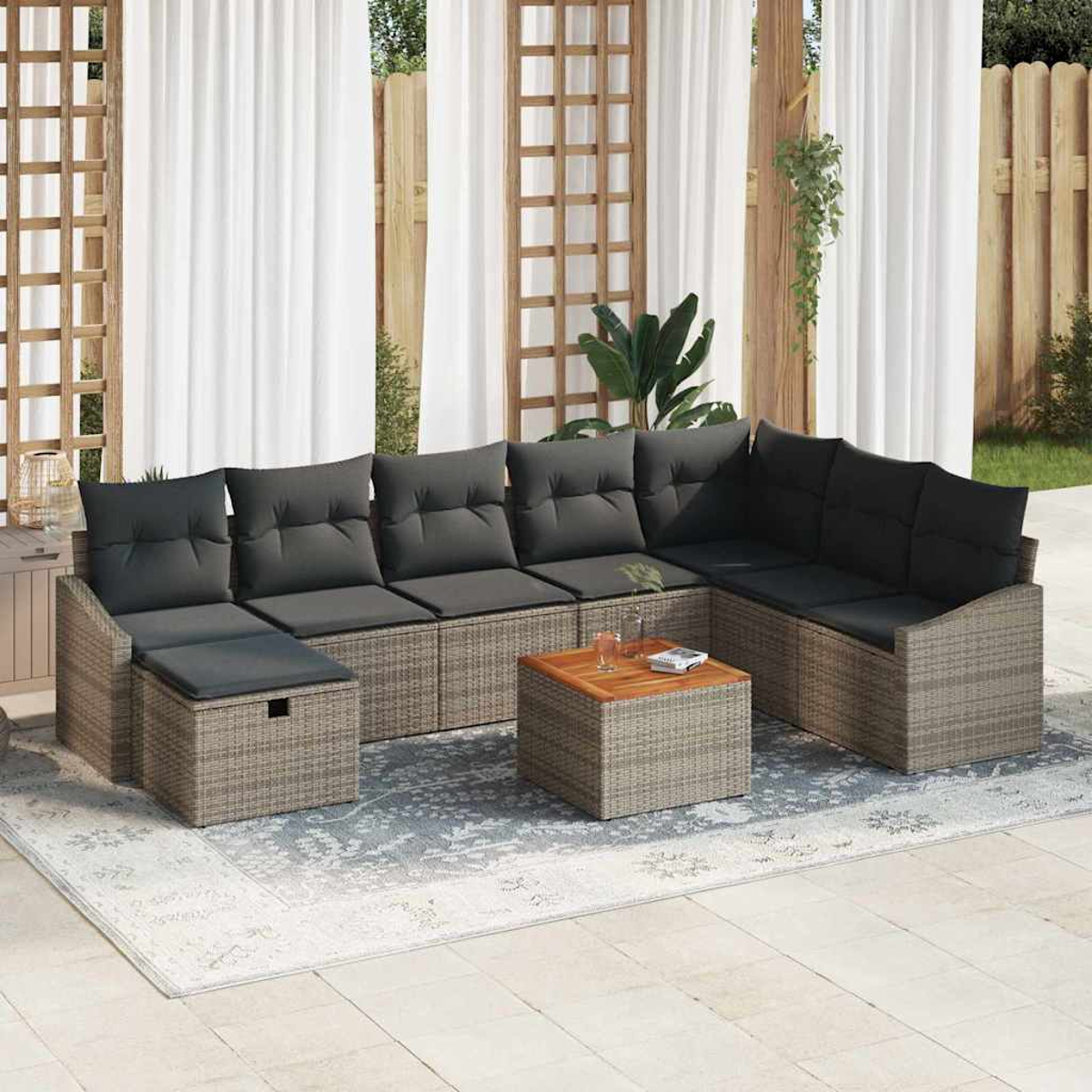 Gartensofa mit grauen Kissen, einem Holztisch und einem Teppich. Weiße Vorhänge und Holzzaun sind im Hintergrund.
