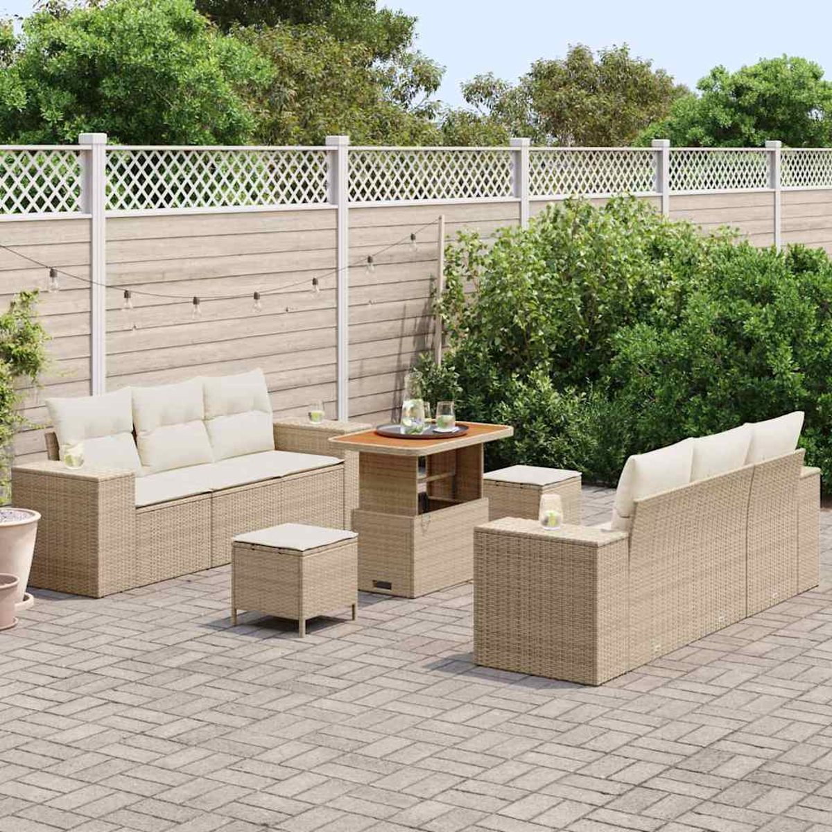 Terrassenset mit Sofa, Stühlen und Tisch. Beigefarbene Korbmöbel mit cremefarbenen Kissen auf einer Ziegelterrasse, umgeben von Grün und einem Zaun.
